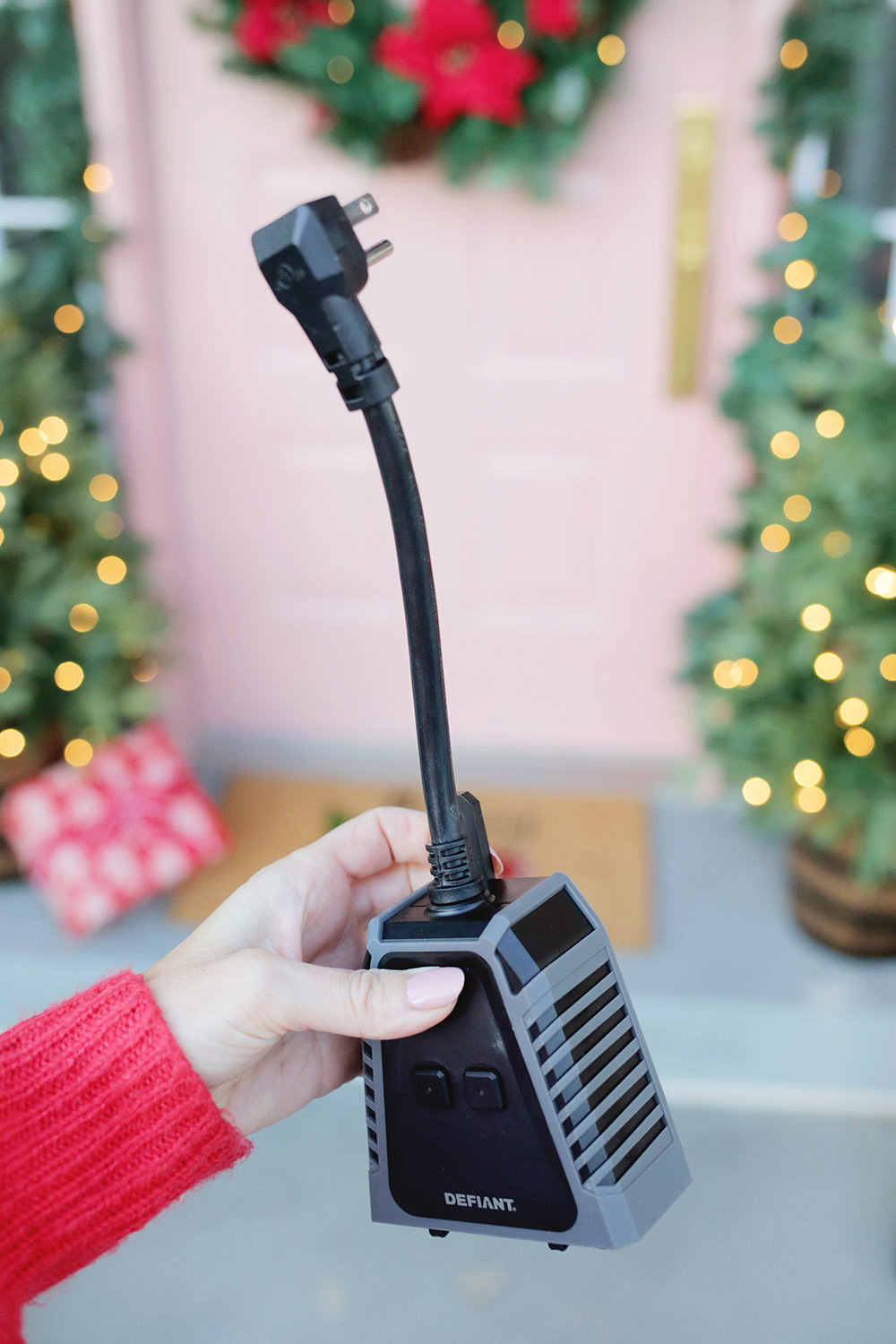 A photo of someone holding a HubSpace Defiant smart plug in front of a decorated front door.
