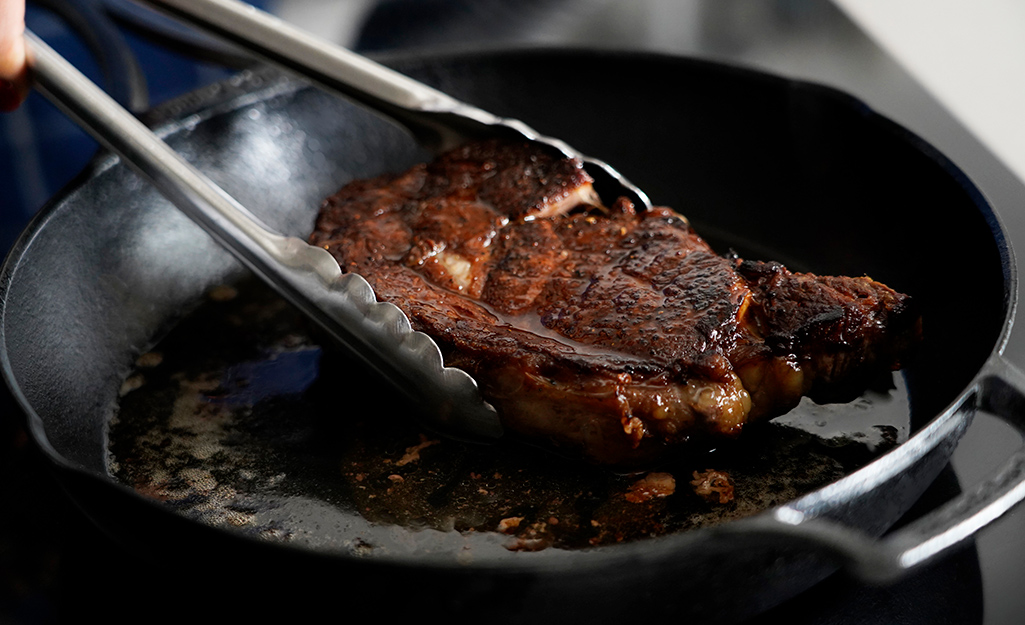 A steak is being seared in a cast iron frying pan. 