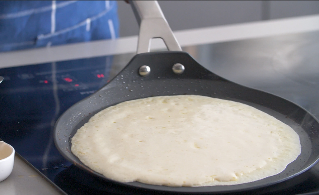 A crepe pan is used to cook a pancake.