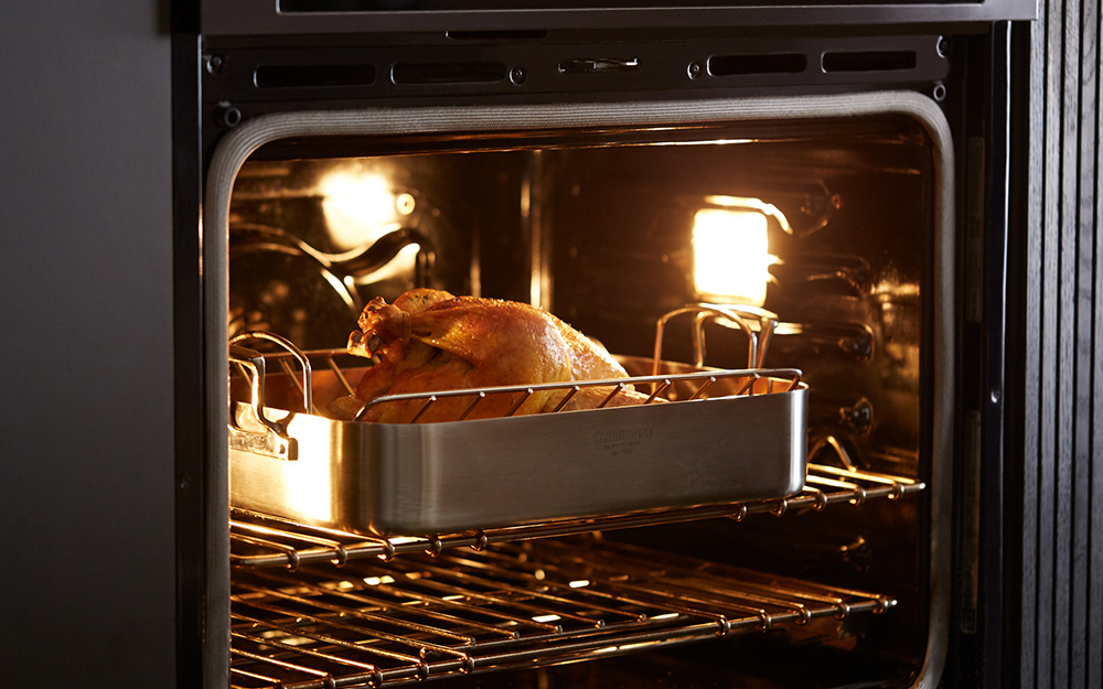 A roasting pan holding a chicken inside an oven.