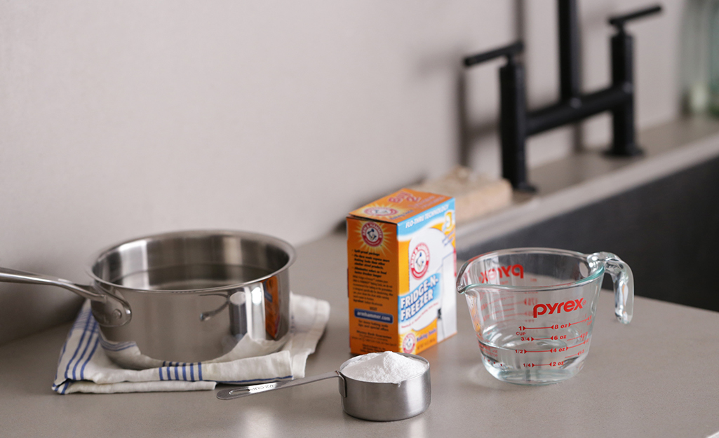 A pot, baking soda and a measuring cup sit on a kitchen countertop.