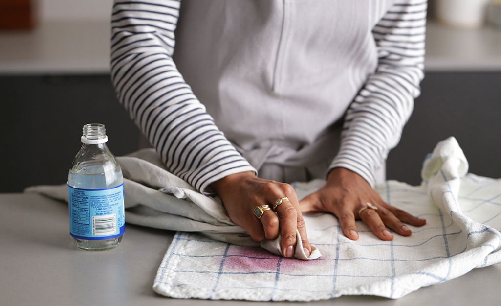 A woman uses club soda to remove a red wine stain from a towel.