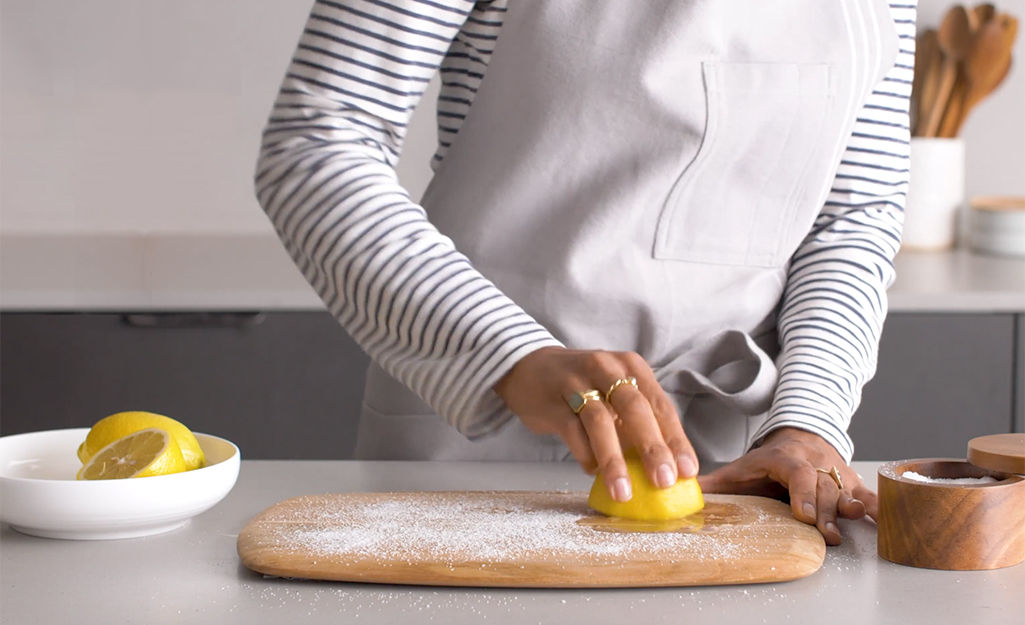 A woman uses a lemon wedge and salt to clean her cutting board.