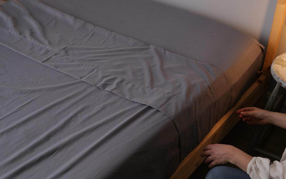 A person tucking in grey sheets on a bed A person tucking in grey sheets on a bed