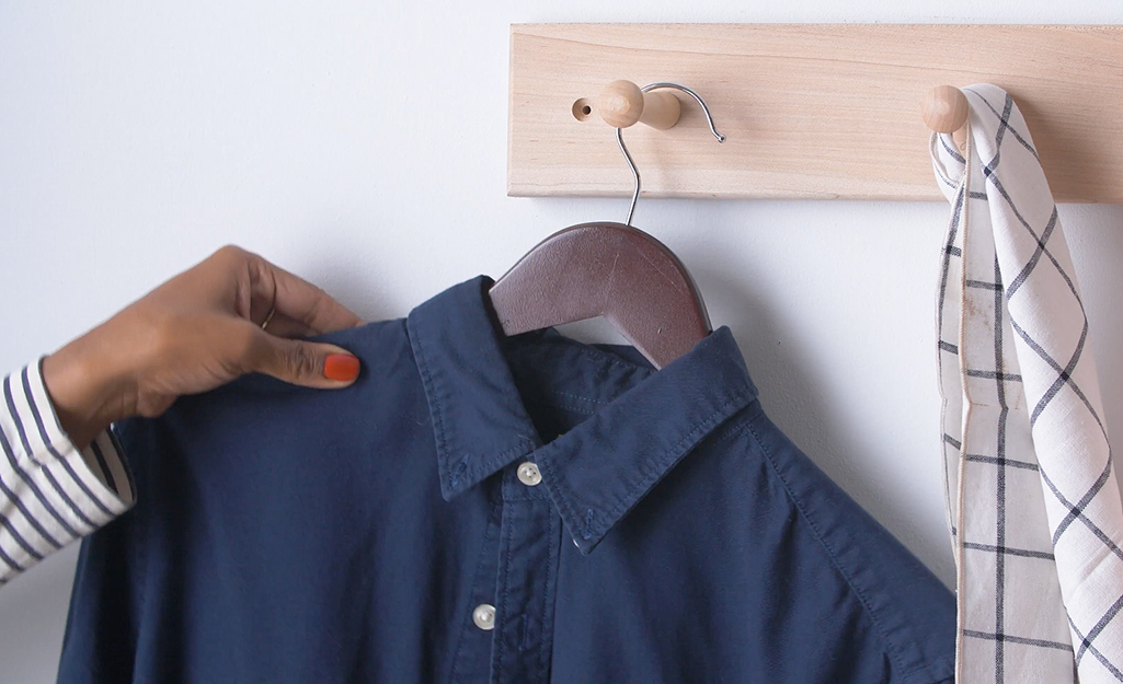 A person hangs a blue shirt on a wood rack