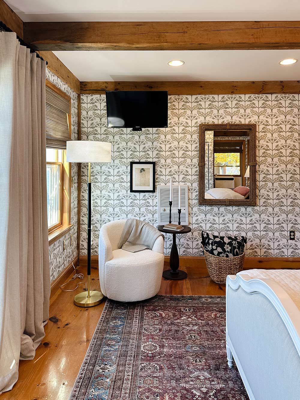 An ivory armchair and side table with a candle stick and rectangle mirror on the wall. An ivory armchair and side table with a candle stick and rectangle mirror on the wall.