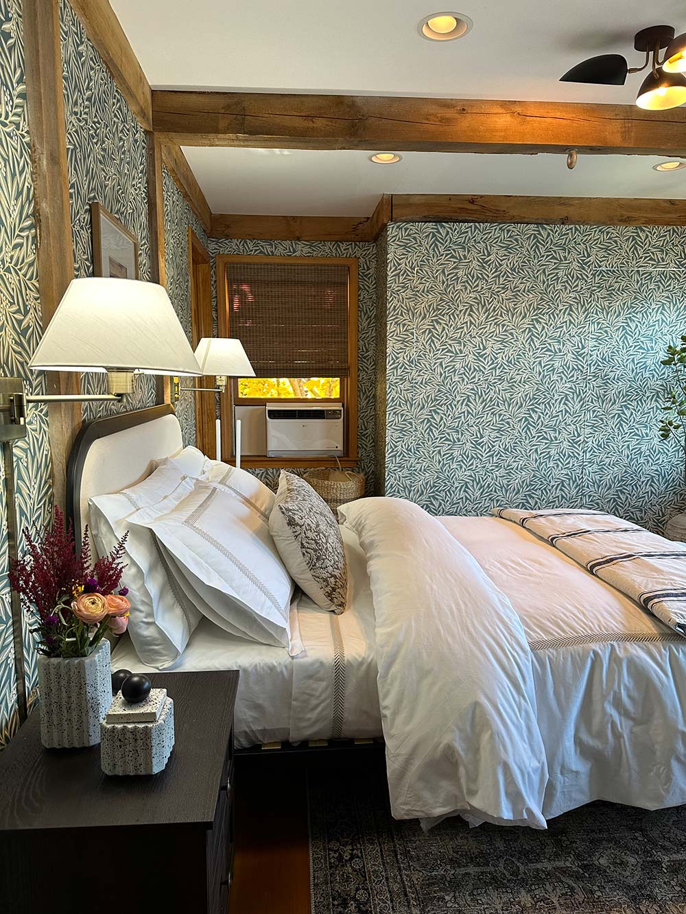 A bed with matching sconces and a side table with flowers. A bed with matching sconces and a side table with flowers.