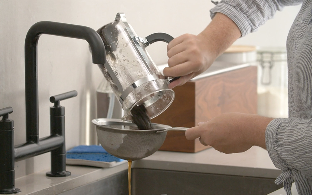 A person straining used coffee grounds from a french press coffee maker.