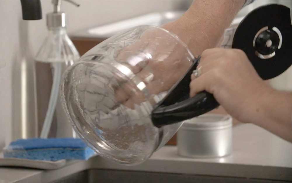 Person cleaning glass coffee carafe.