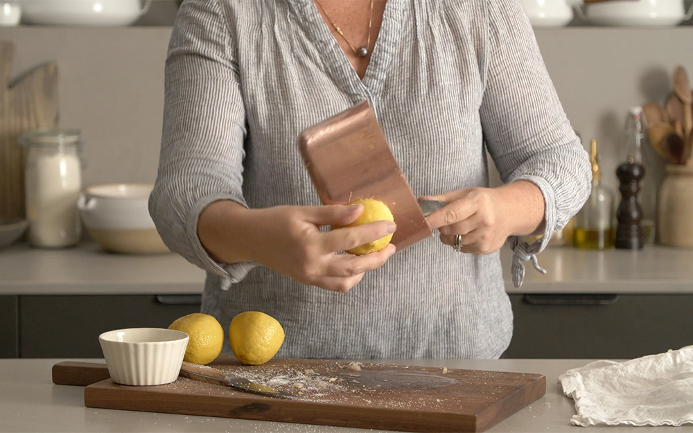 A person rubs lemon juice on a copper saucepan.