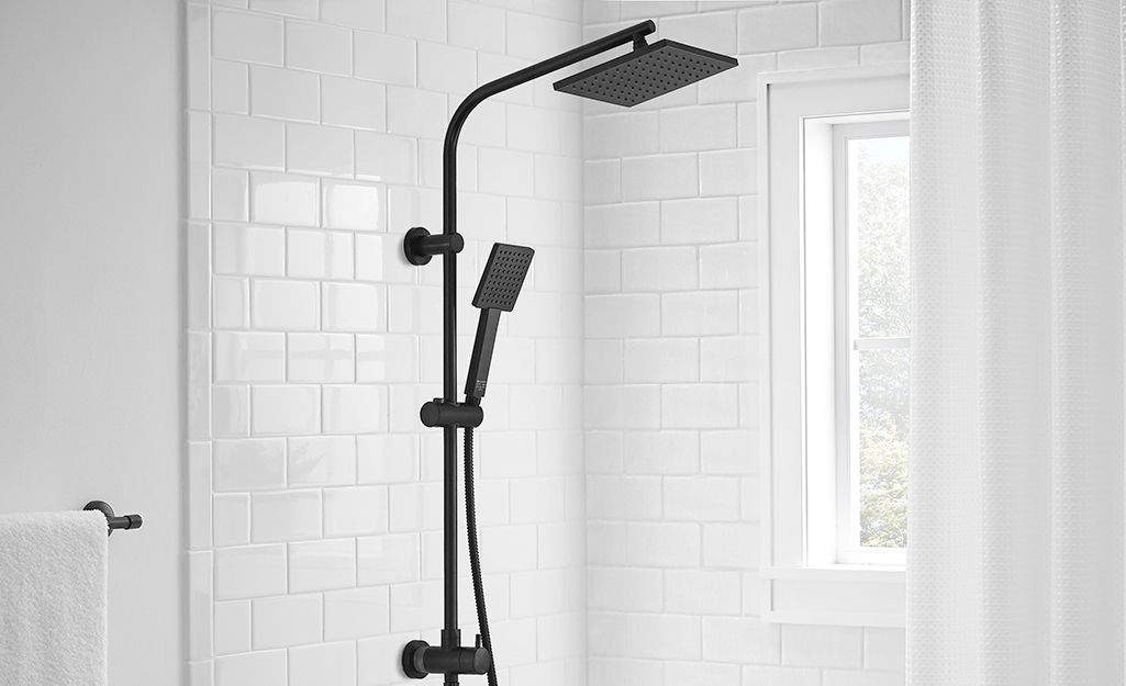 A black shower head and sprayer hanging in a white tile bathroom.