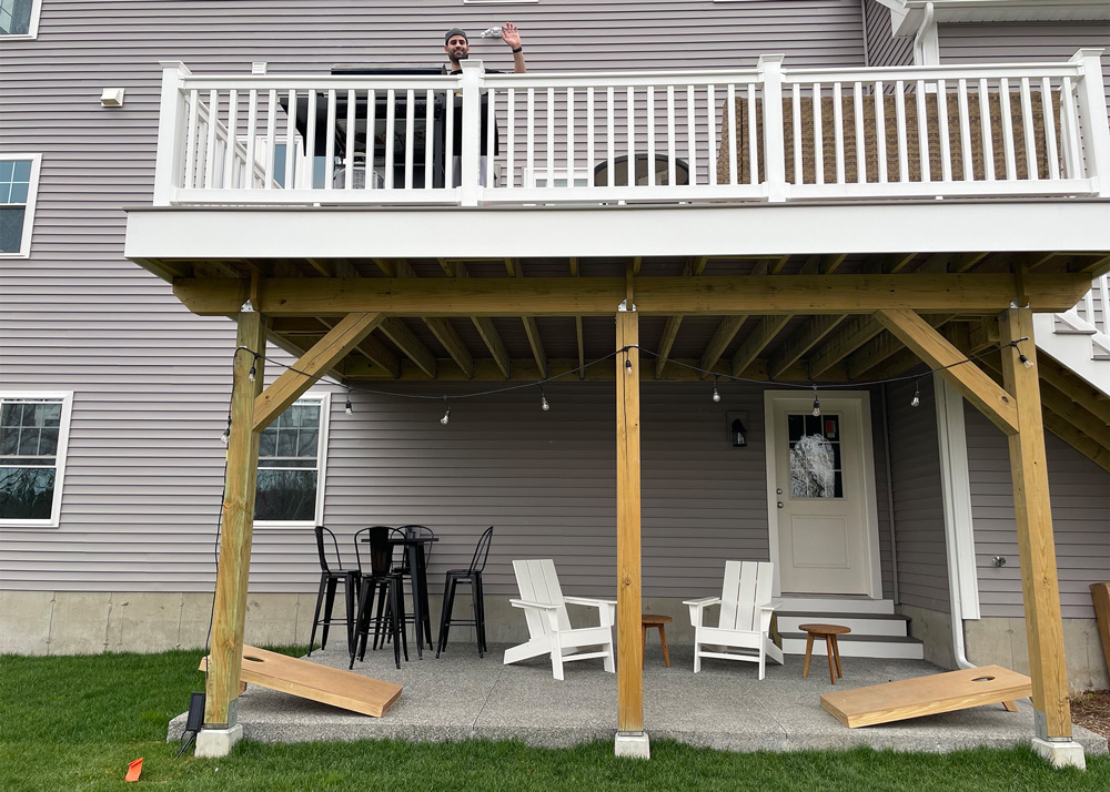 A backyard patio supported by a wooden structure with a man standing at the top of the patio waving