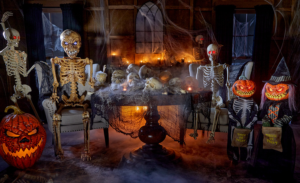A spooky display of skeletons and pumpkins at a dining table.