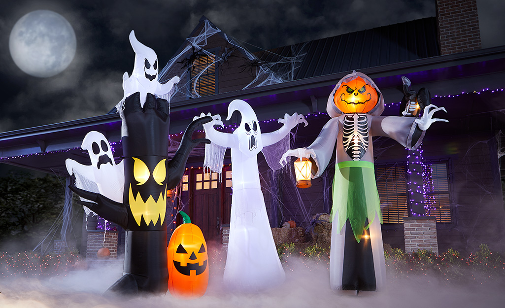 Inflatable ghosts and jack o' lanterns in front of a Halloween decorated house.