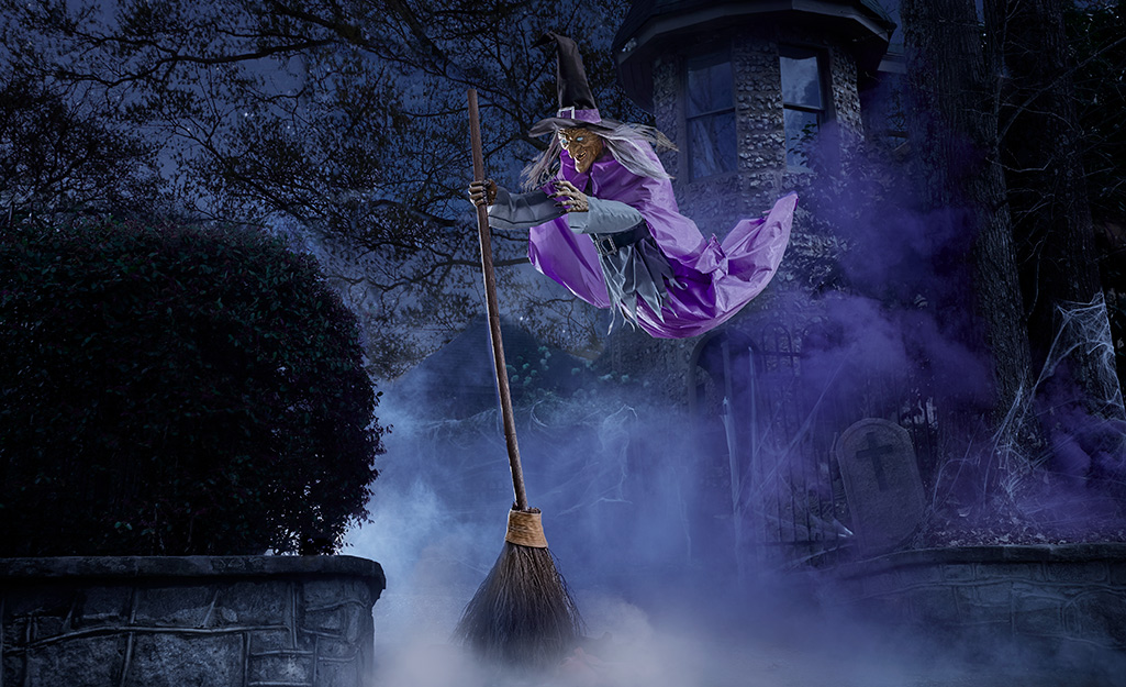 A witch rises on a broom above a fog-shrouded landscape.