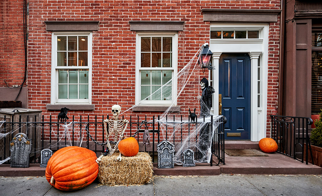 A DIY Halloween scene of a skeleton, hay bale and pumpkins outside a home.