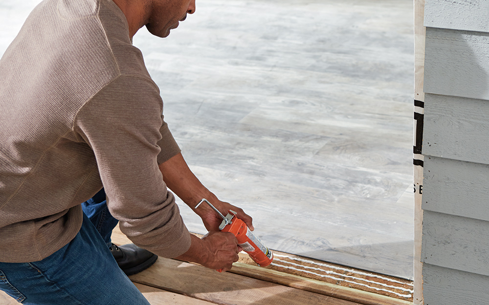 A man caulks the bottom opening of a frame for sliding door installation.