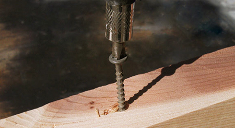 A person turns a screw into a piece of wood.