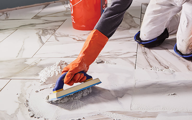 A close up of a person using a grout float to apply grout to tile.