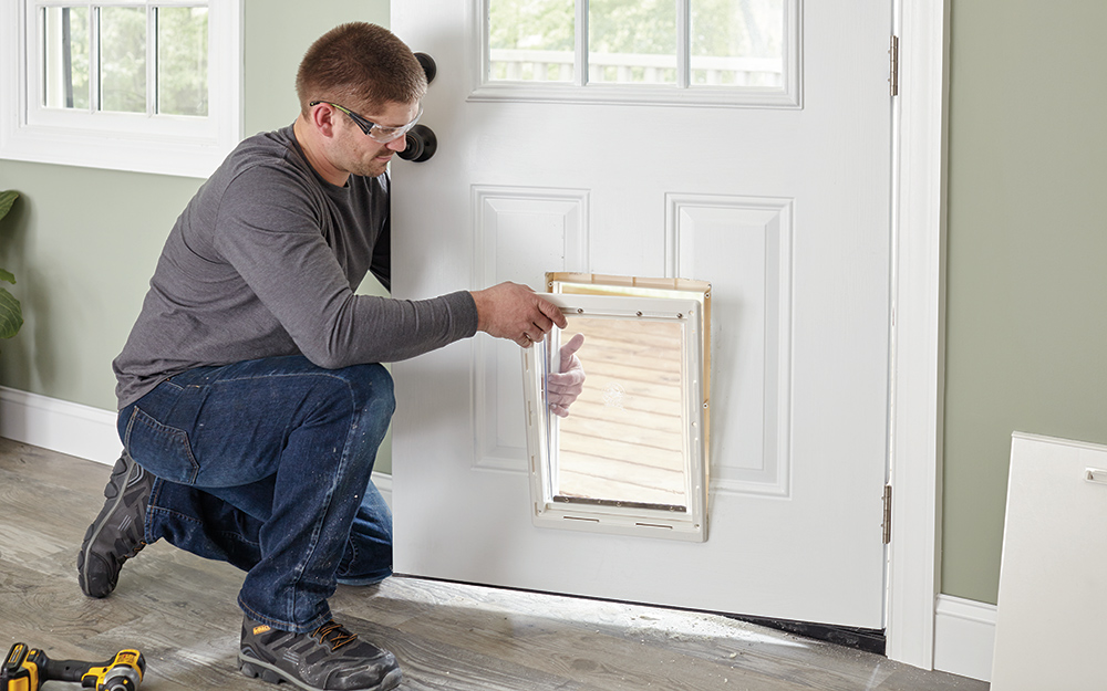 A man placing the frame of a dog door into an exterior door