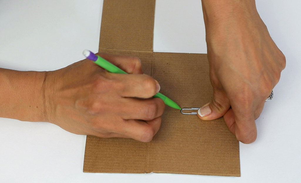 Someone drawing the shape of a paper clip onto a piece of cardboard. Someone drawing the shape of a paper clip onto a piece of cardboard.