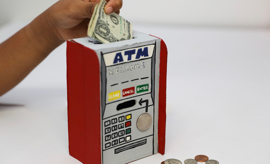 Someone putting money in a painted DIY ATM bank.