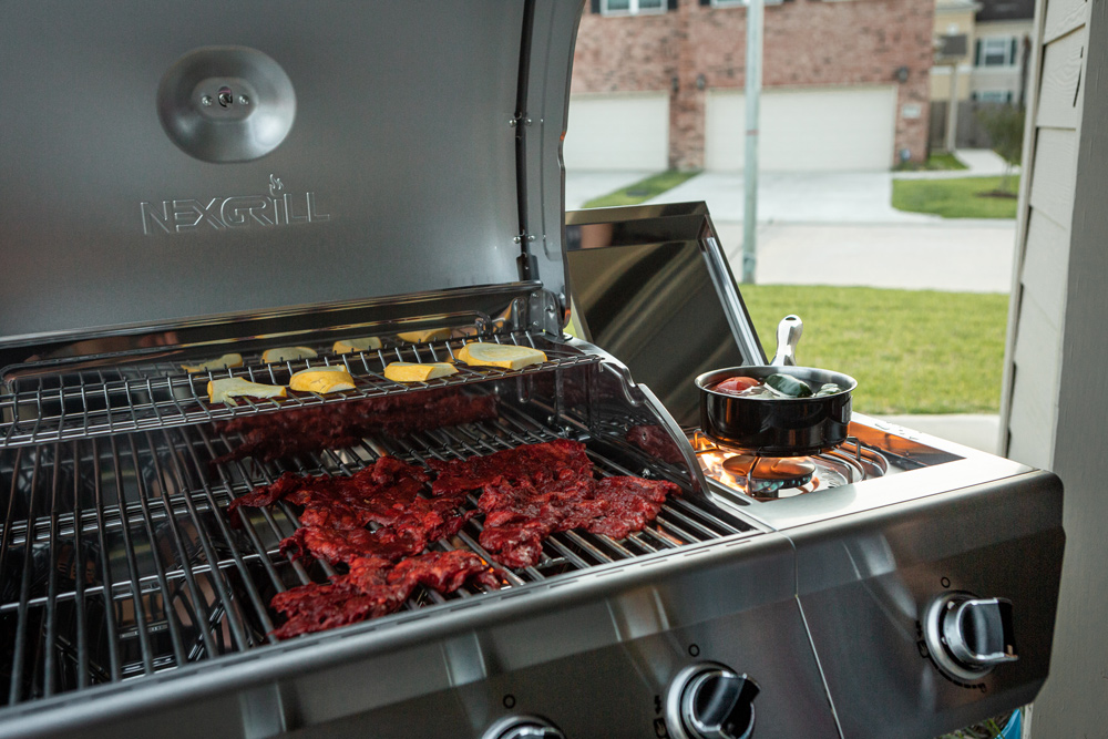 Grill with meat, vegetables, and a pot with vegetables to the right side.