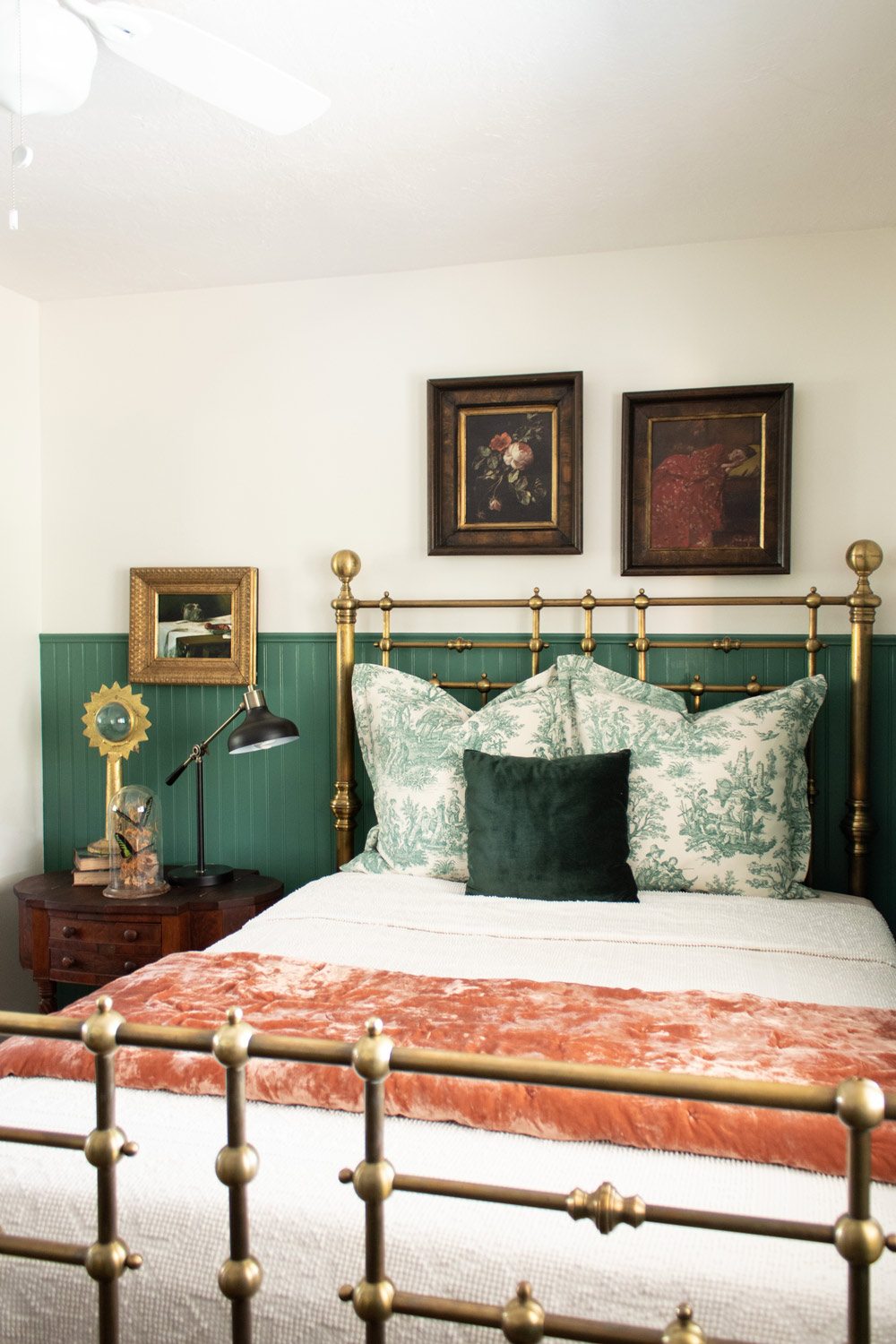A decorated white room with a green beadboard, bed frame and three picture frames.