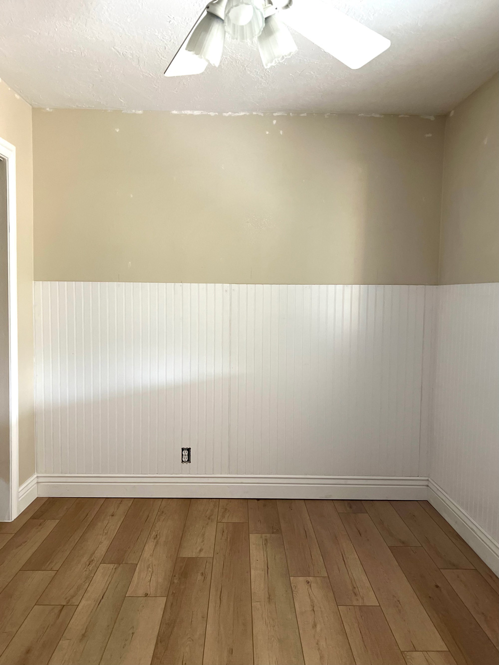 A beige room with white beadboard and ceiling fan.
