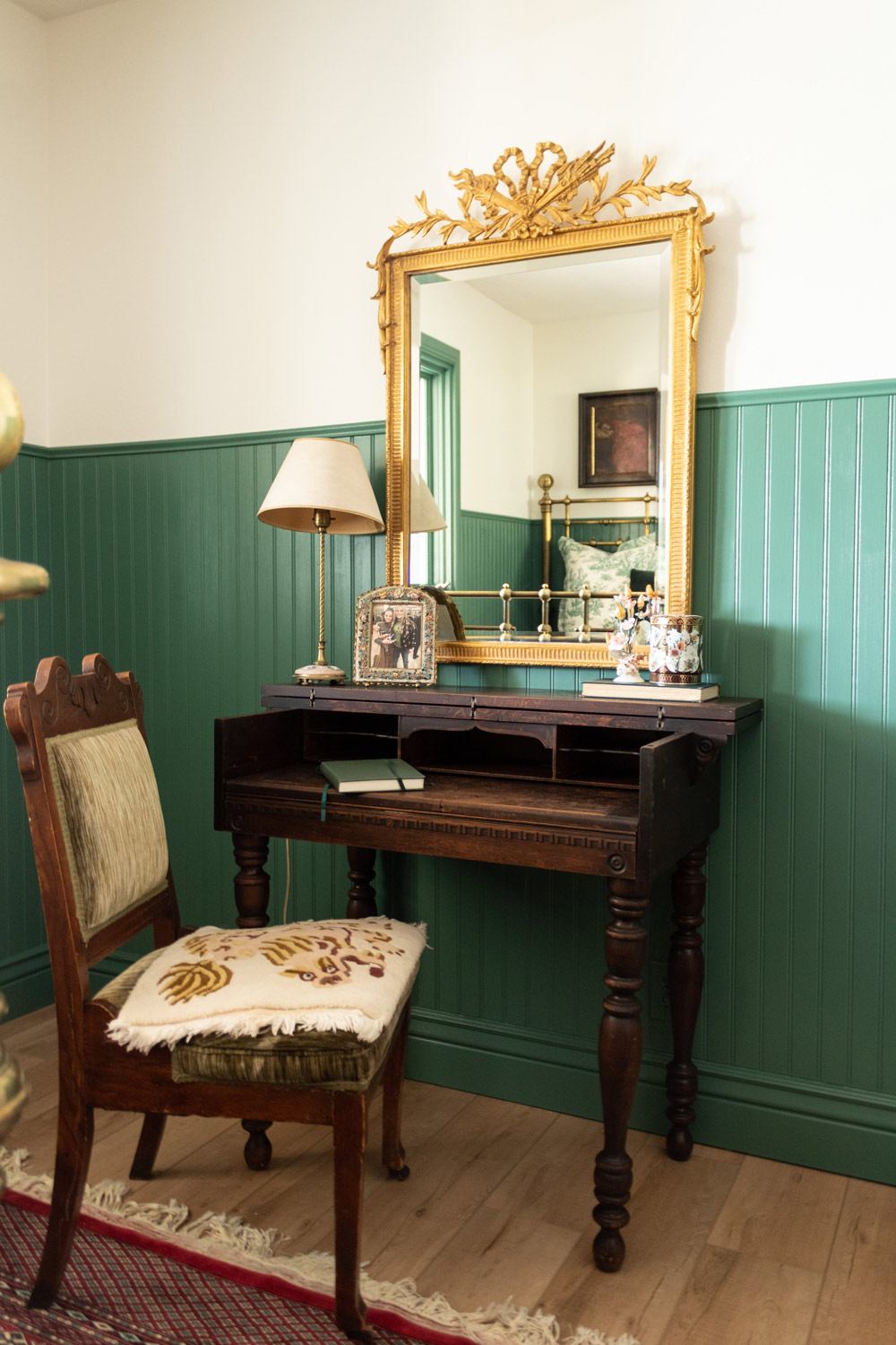 A wooden desk and chair with a gold framed mirror.