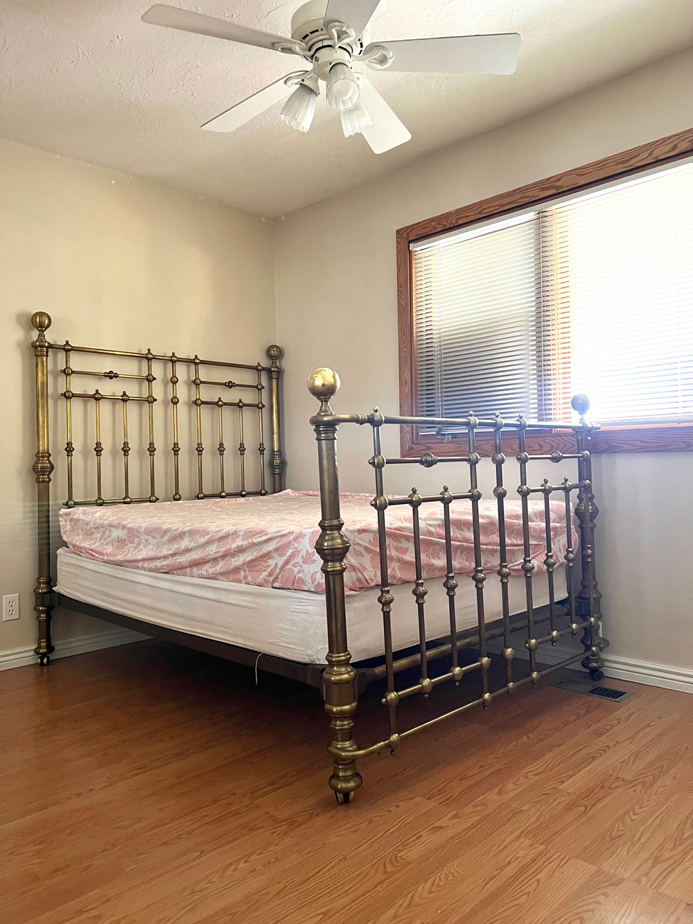 A beige room with a bed frame and ceiling fan.