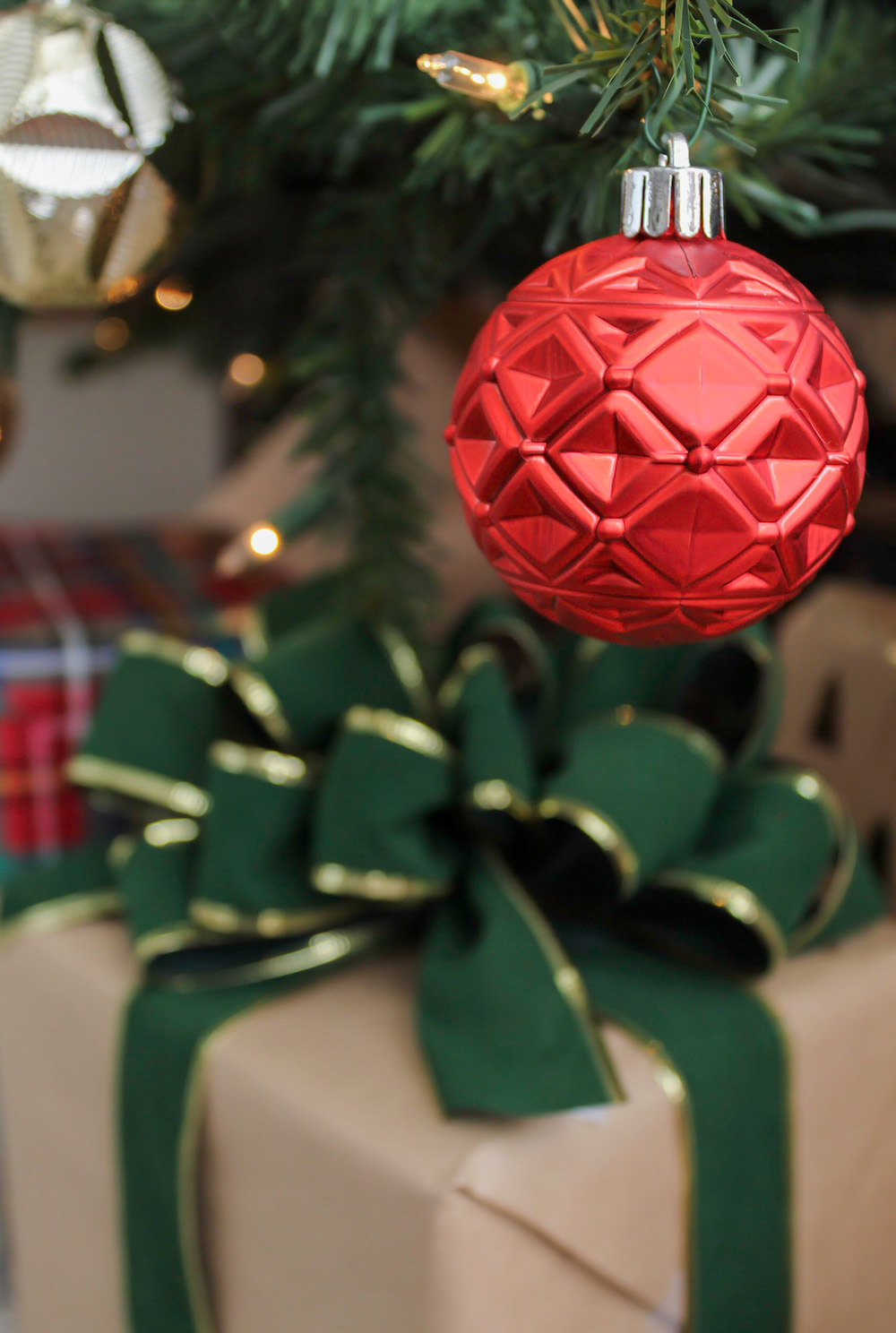 Close up of a red ornament hanging from tree with a beige and green gift in the background