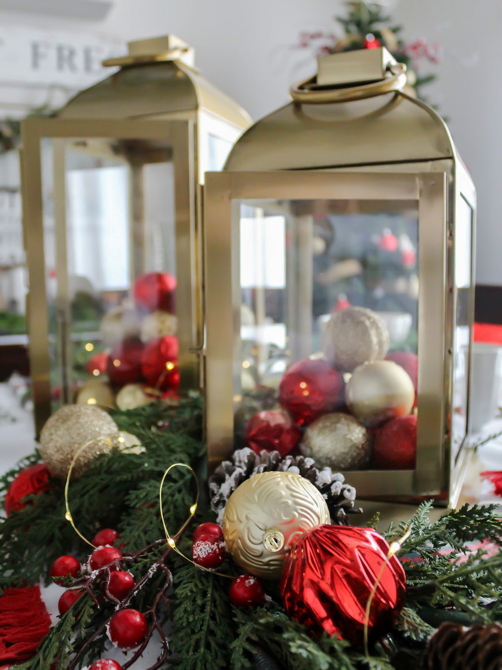 Close up of two gold lanterns filled with red and gold ornaments surrounded by green, red and gold holiday decor