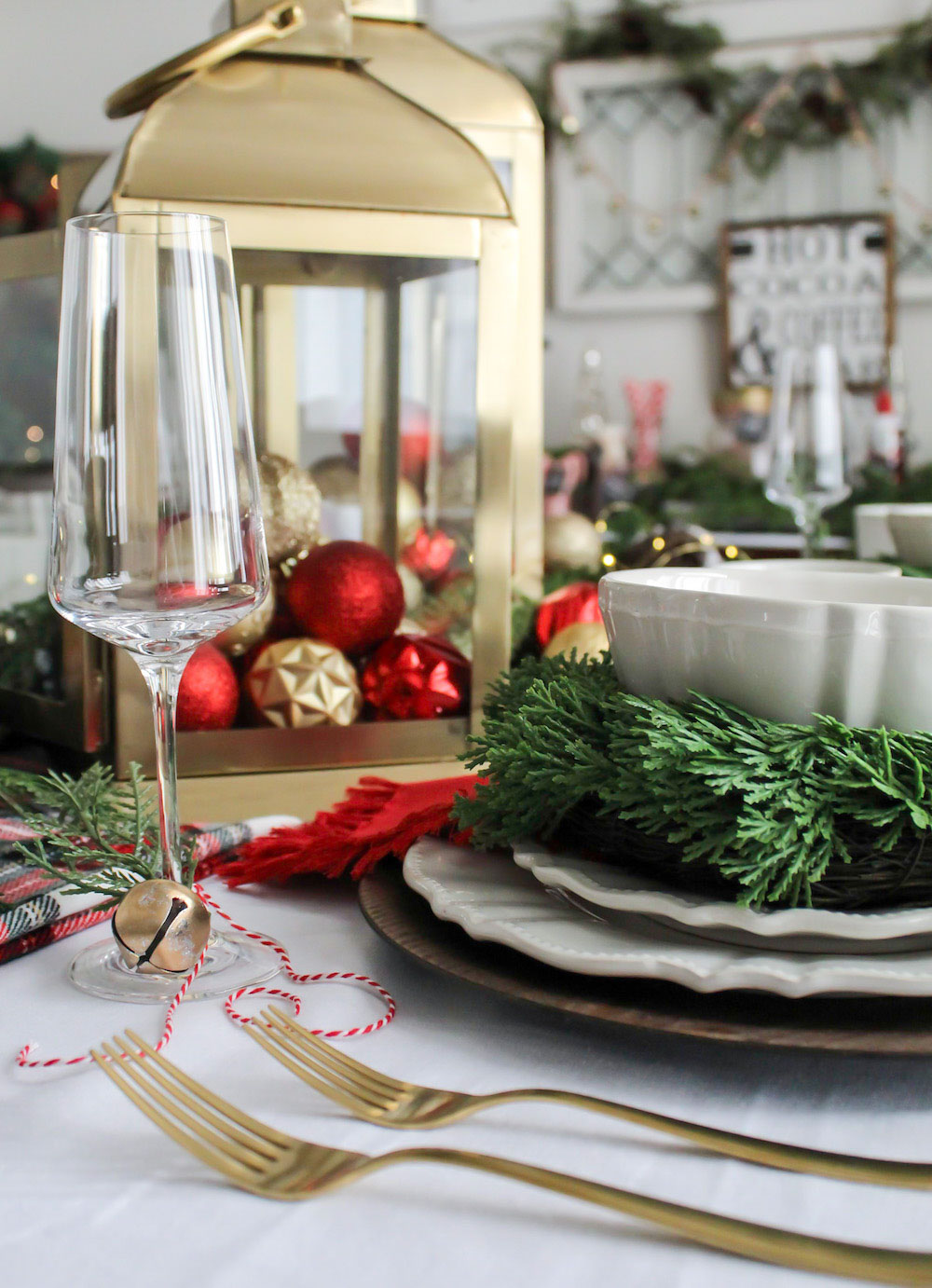 Close up shot of red, gold and green decorated dining room table contains wine glass, gold cutlery and dinner plates and bowl
