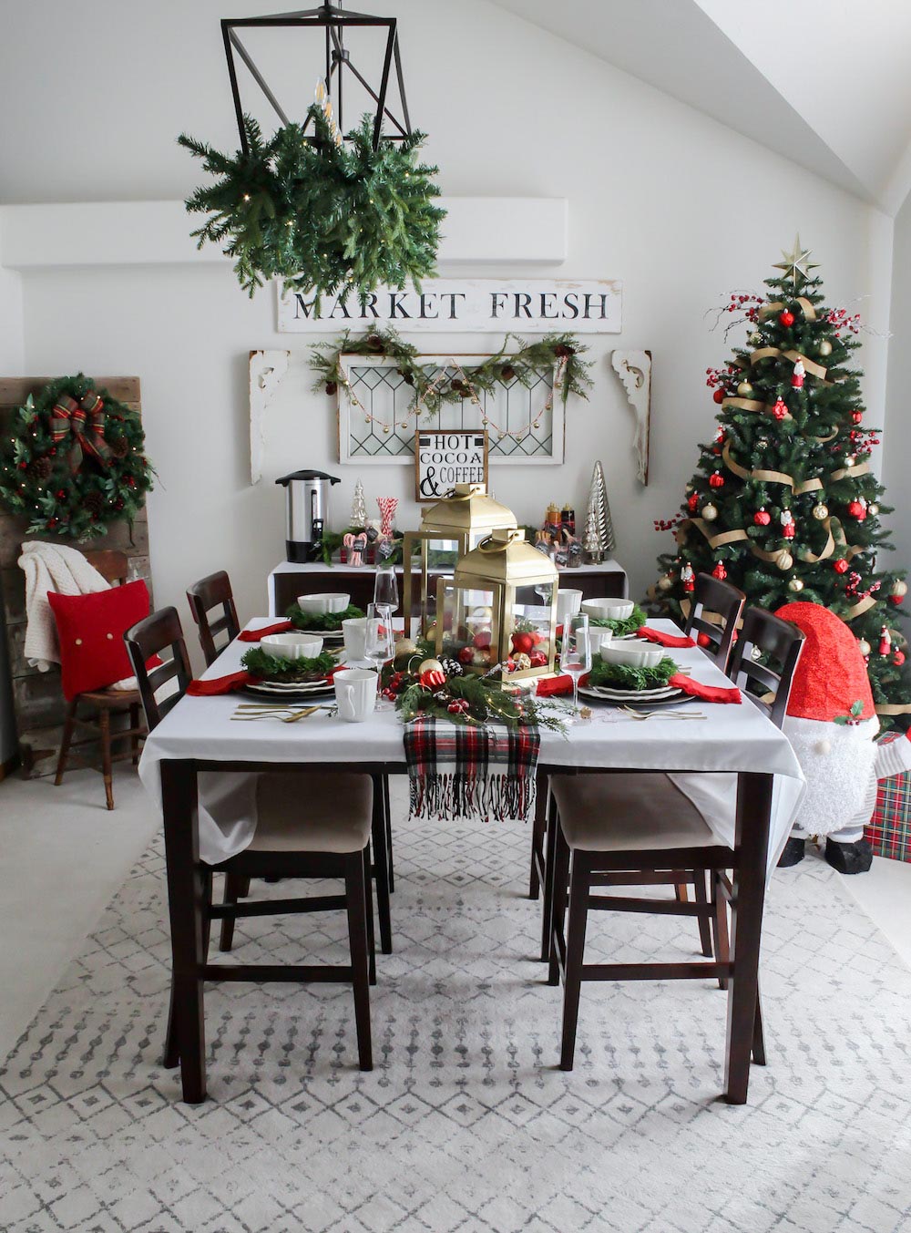 Centered dining room table decorated with holiday decor with Christmas tree in the back right corner