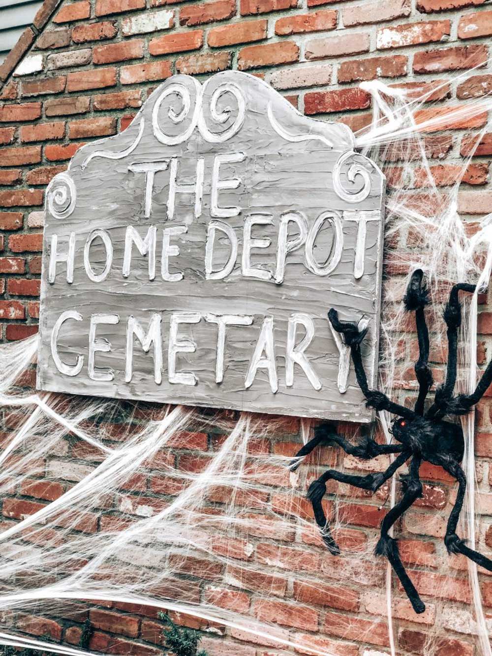 A sign that reads The Home Depot Cemetery with spider webs.