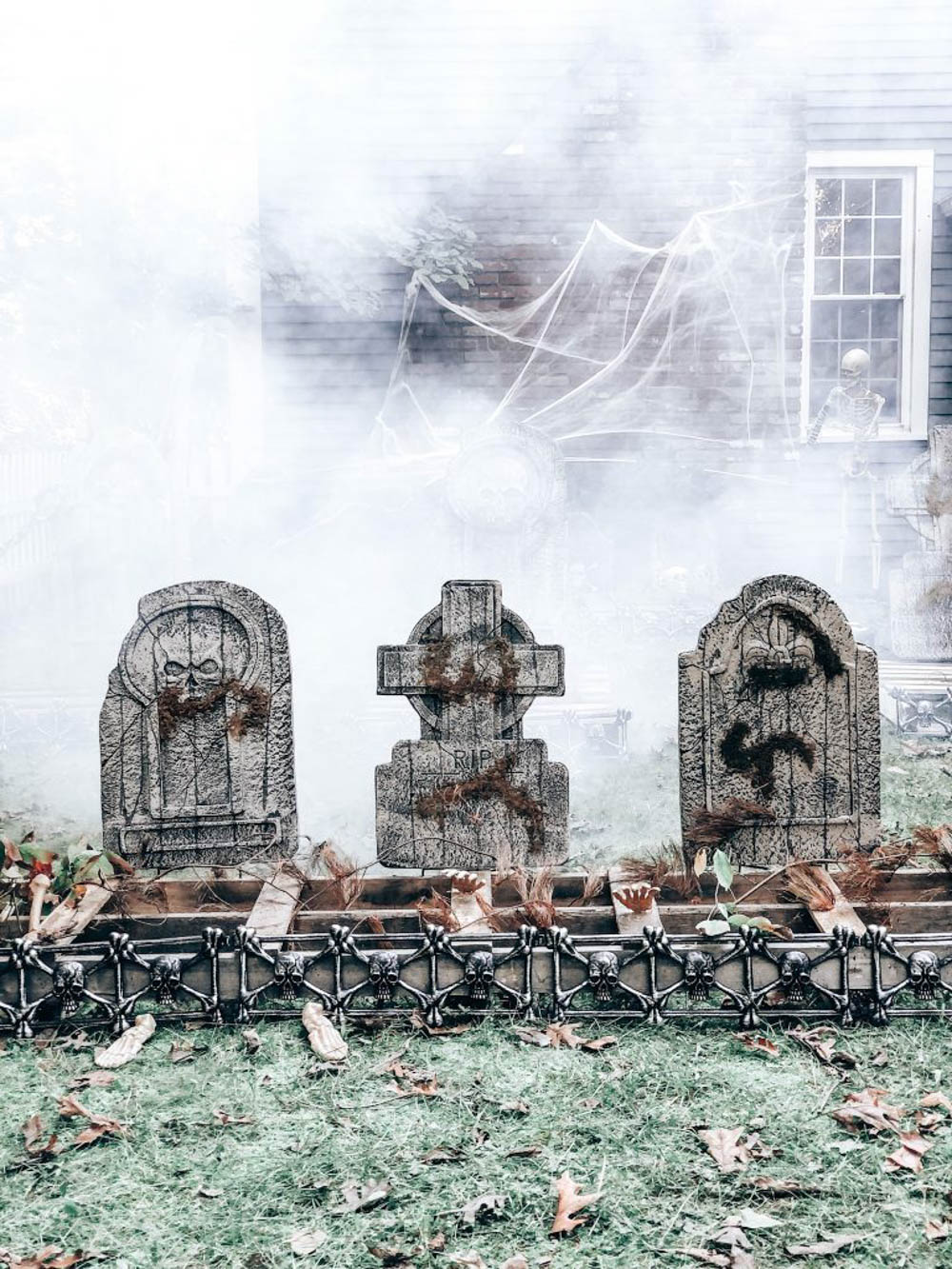 A trio of tombstones sitting in a foggy graveyard.