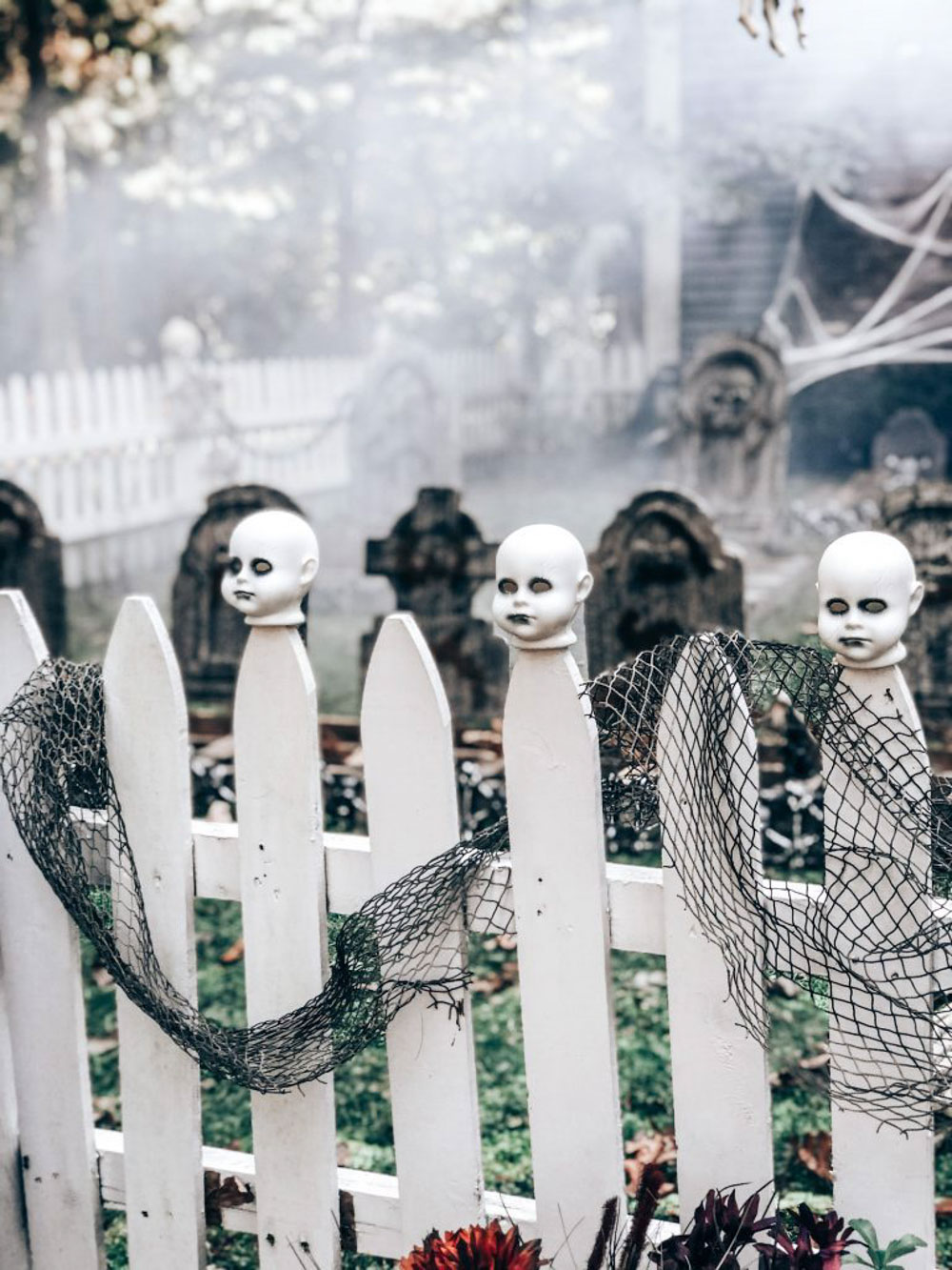 A group of doll heads sitting on top of a white picket fence.