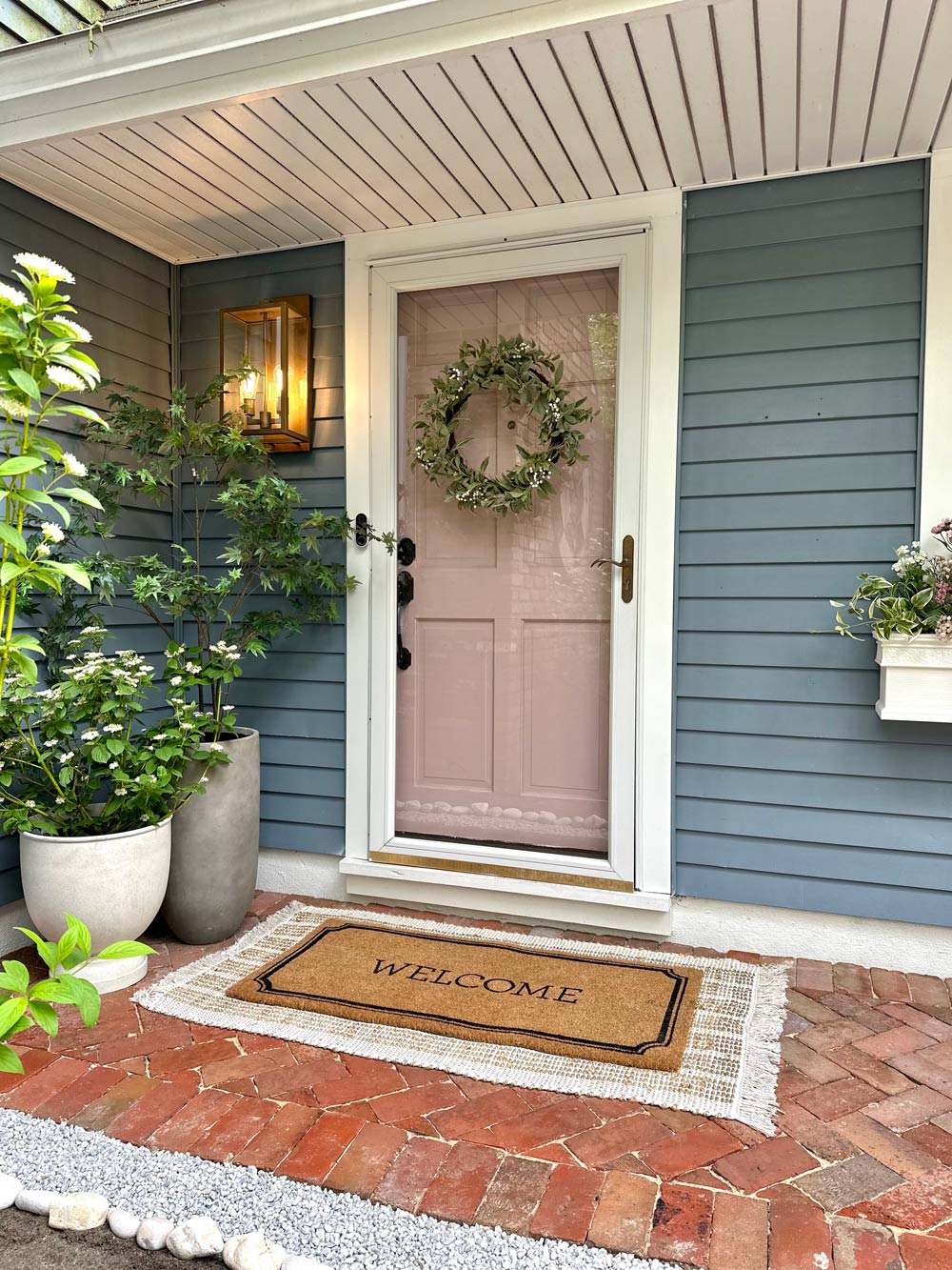 Brick front porch with blush door and welcome mat. 