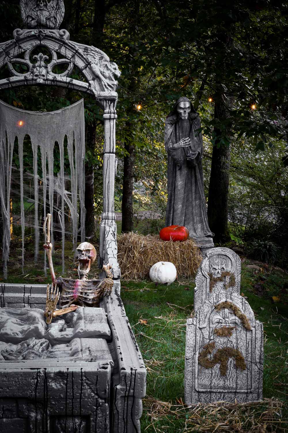A spooky cemetery statue holding an hourglass standing behind a crypt and tombstone.