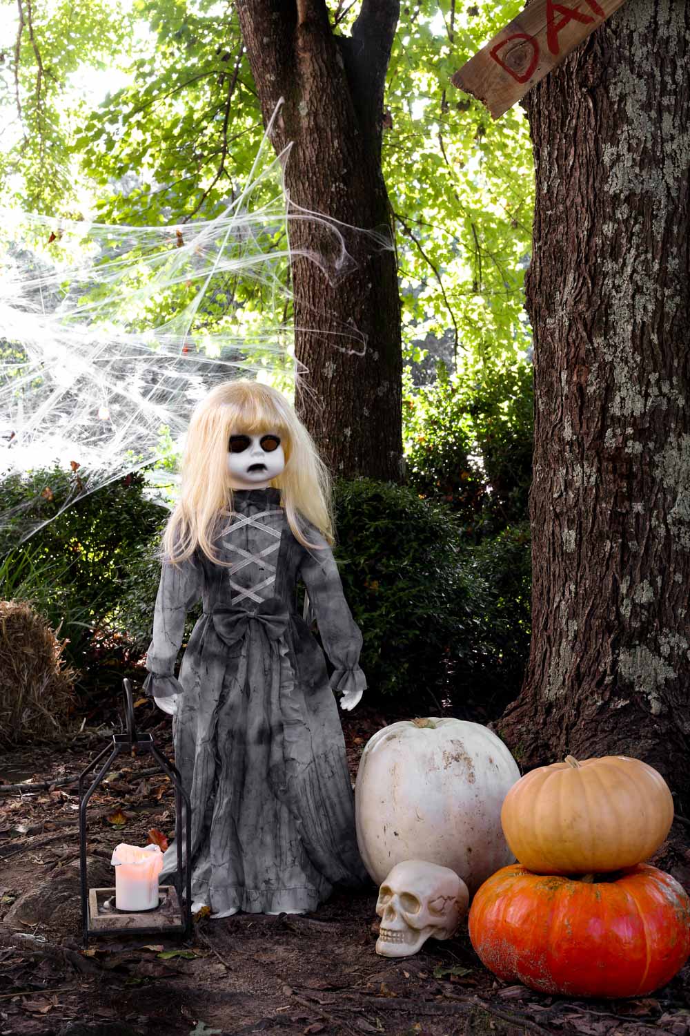 A ghostly doll with a white face and red eyes standing next to a skull and pumpkins.