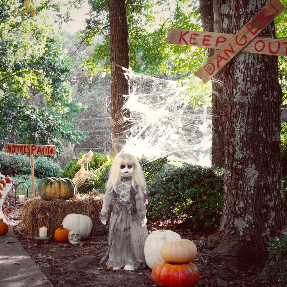 A ghostly doll standing in the woods surrounded by keep out and danger signs.