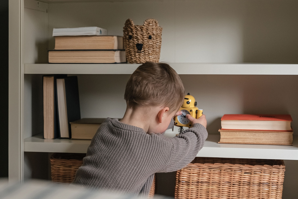 A boy playing with a yellow robot in front of a bookshelf.