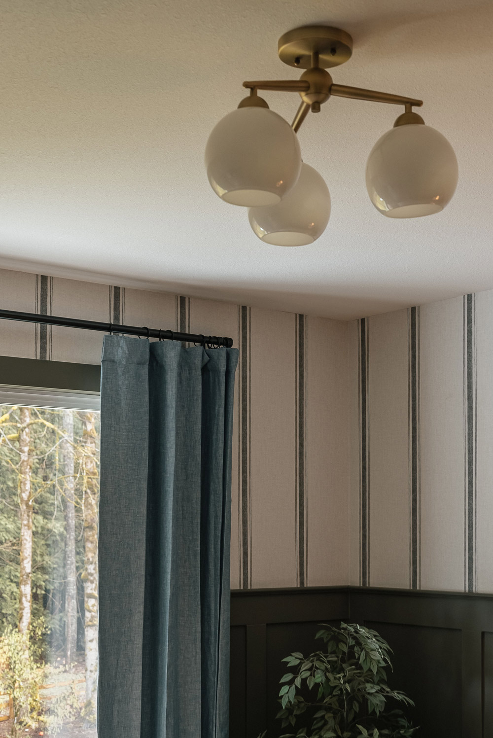 3-light fixture on the ceiling, striped wallpaper, and a window with a curtain.
