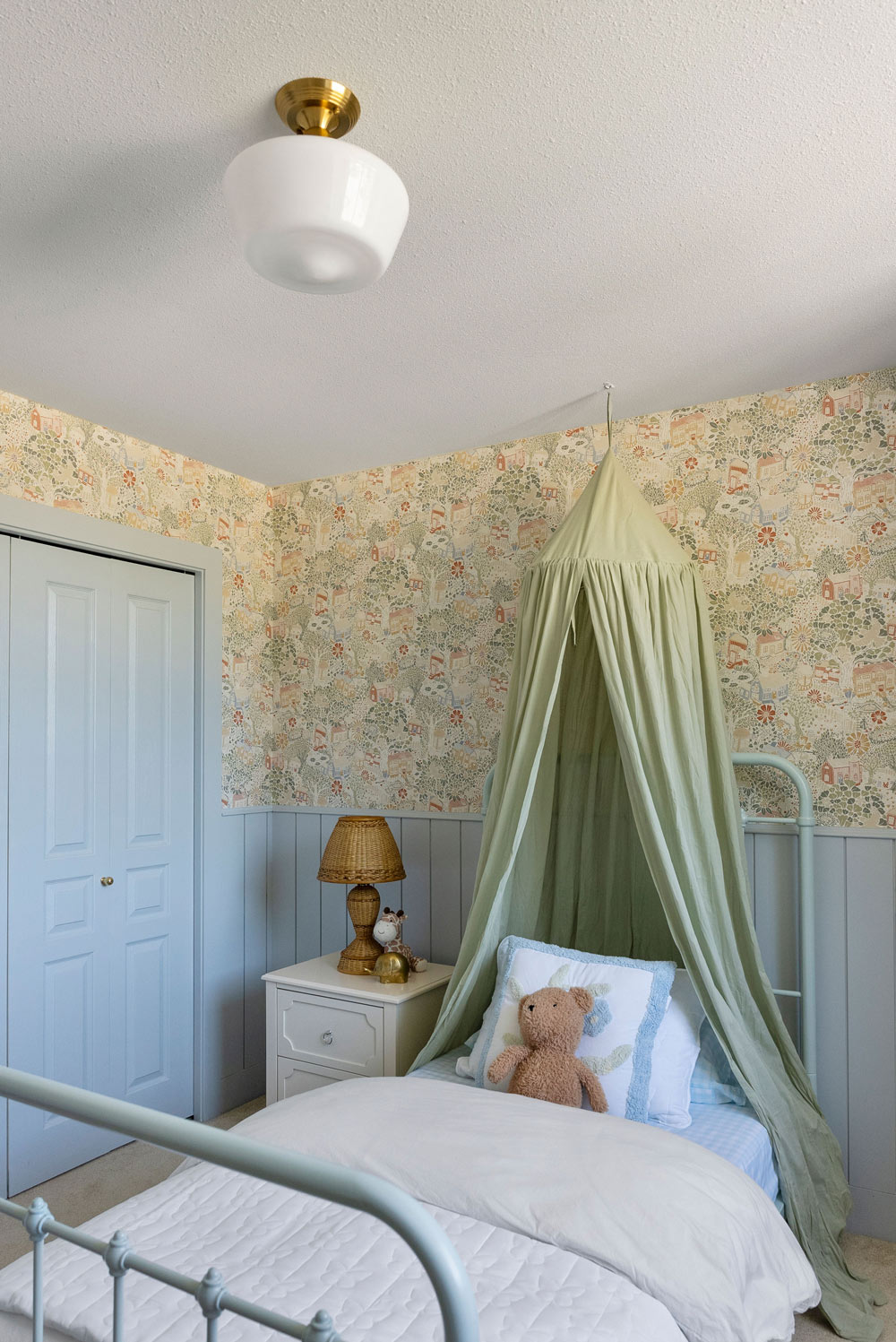Right-side view of a completed kid’s bedroom with floral wallpaper, and bed styled with throw pillows and a teddy bear. Right-side view of a completed kid’s bedroom with floral wallpaper, and bed styled with throw pillows and a teddy bear.