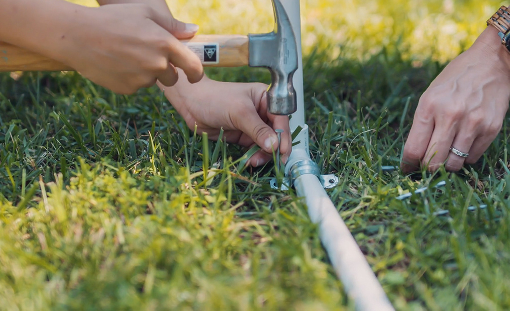 A person anchoring a DIY kids sprinkler to a lawn with a U-bolt.