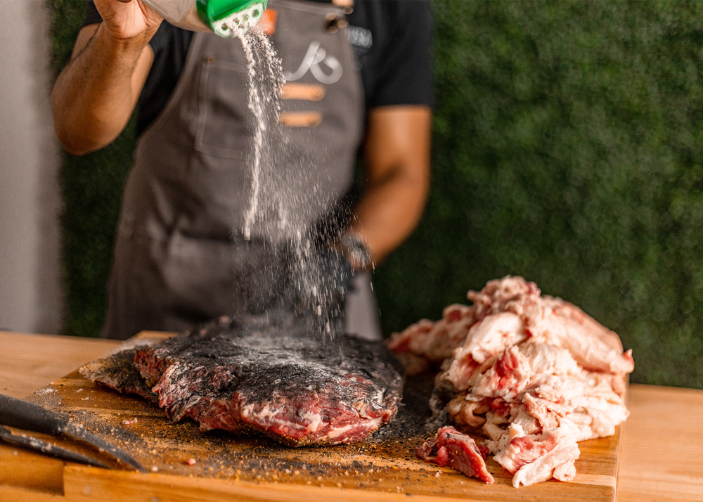 Chef seasoning brisket on cutting board. Chef seasoning brisket on cutting board.