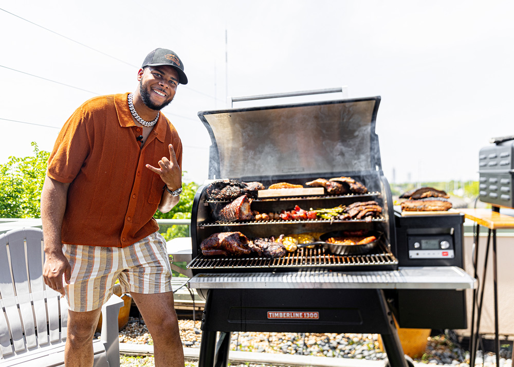 Chef JRob standing next to a grill full of food. Chef JRob standing next to a grill full of food.