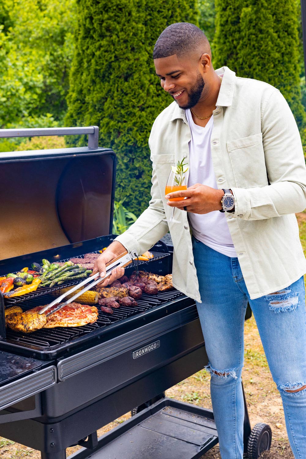 A man grilling food while holding a mocktail.