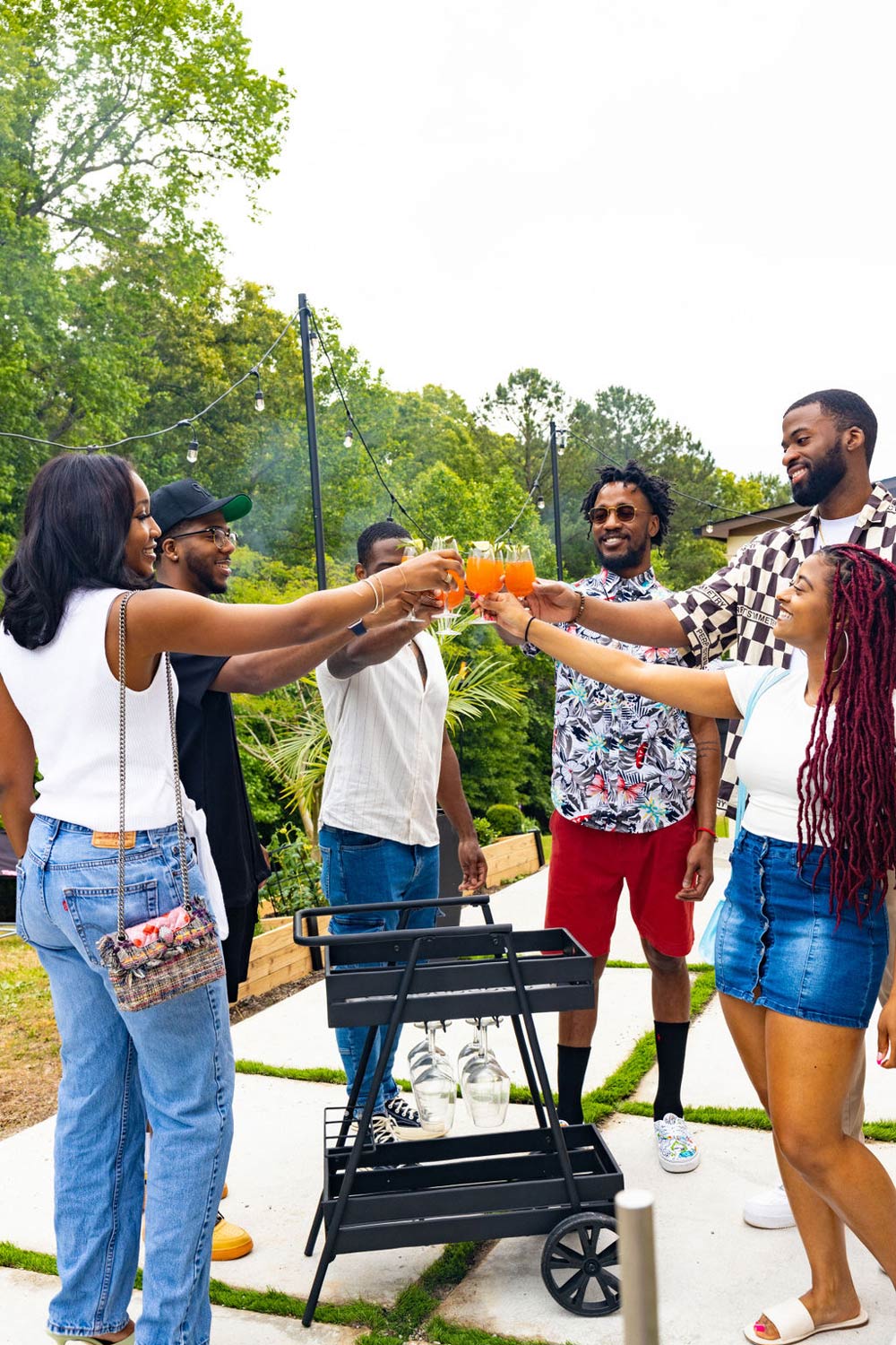 A group of people staniding around a bar cart toasting mocktails. A group of people staniding around a bar cart toasting mocktails.